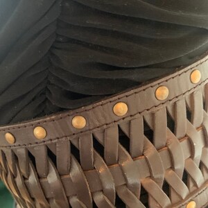 Peut inclure: Une ceinture en cuir marron avec un motif tissé et des accents métalliques dorés. La ceinture est portée sur une robe noire.