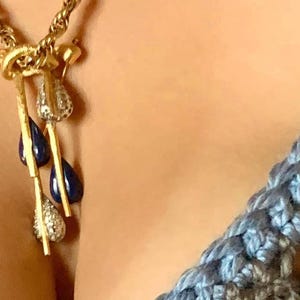 May include: A gold necklace with a pendant featuring three teardrop-shaped blue stones and a smaller diamond-shaped stone.