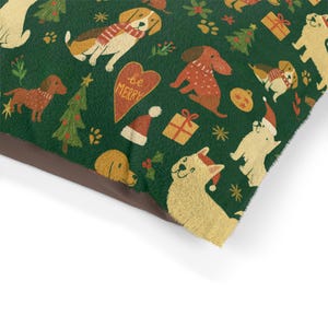 Peut inclure: Un coussin pour animaux de compagnie vert festif avec un motif répété de chiens portant des chapeaux et des écharpes de Père Noël, ainsi que des sapins de Noël, des cadeaux et les mots "be MERRY" sur un cœur. Le coussin a une bordure marron.