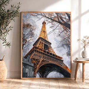 May include: A framed painting of the Eiffel Tower in Paris. The artwork features the iconic tower in shades of gold and brown against a backdrop of gray and white, with bare tree branches. The painting is displayed in a room with natural light.
