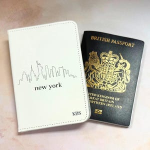 May include: A white passport holder featuring a New York skyline and the word "new york". Beside it, a British passport with gold detailing and the words "British Passport".