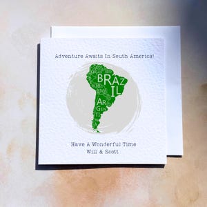 May include: A white greeting card featuring a green map of South America, with country abbreviations. The card includes the phrases "Adventure Awaits In South America!" and "Have A Wonderful Time Will & Scott."