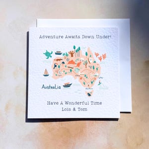May include: A square greeting card featuring a light peach map of Australia with colourful illustrations of wildlife, boats, and landmarks. The text reads Adventure Awaits Down Under!, Australia, Have A Wonderful Time, and the names Lois & Tom.