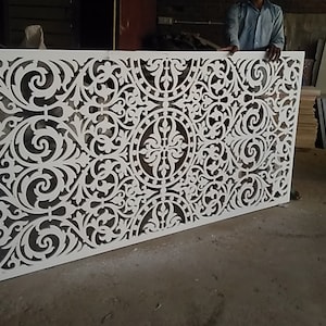 May include: A white decorative panel with a intricate, laser-cut design featuring a repeating pattern of swirling floral motifs. The panel is made of a lightweight material and has a smooth, polished finish.