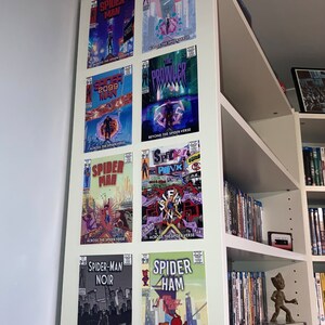 Puede incluir: Una estanter&iacute;a blanca con ocho portadas de c&oacute;mics que presentan diferentes personajes de Spider-Man. Las portadas est&aacute;n dispuestas en dos filas de cuatro. Las portadas son todas de las pel&iacute;culas "Spider-Man: Across the Spider-Verse" y "Spider-Man: Beyond the Spider-Verse". Las portadas presentan a Spider-Man, Spider-Gwen, Spider-Man 2099, Spider-Punk, Spider-Man Noir y Spider-Ham.
