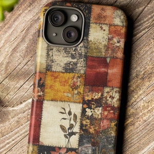 May include: A phone case with a patchwork design featuring various shades of brown, red, and yellow. The case has a floral pattern and a camera lens cutout.