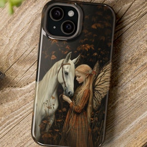 Puede incluir: Una funda de teléfono con un caballo blanco y un hada con alas. El hada lleva un vestido marrón y tiene el pelo largo y rubio. El fondo es un bosque oscuro con hojas de otoño.