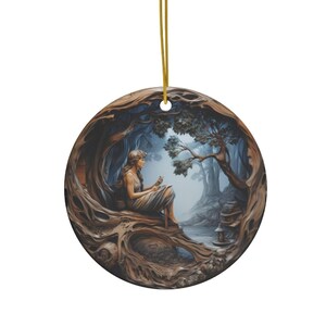 May include: Round ceramic ornament featuring a serene forest scene. A woman in a flowing dress sits on a tree branch, sketching. The artwork is framed by a dark brown, tree-like border, with a gold string for hanging.