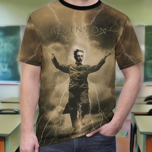 May include: A brown t-shirt with a graphic print of Nikola Tesla standing in a storm cloud with lightning bolts. The text "ASCENSION" is printed above Tesla.