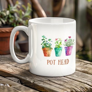 May include: White ceramic mug with a colorful illustration of three potted plants and the text "POT HEAD".