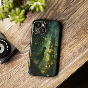 May include: A green and black phone case with a fairy silhouette standing in a forest with glowing lights. The case has a camera lens cutout.