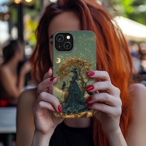 May include: A phone case with a green, blue, and black design featuring a woman in a long dress standing under a tree with a crescent moon and stars in the background.