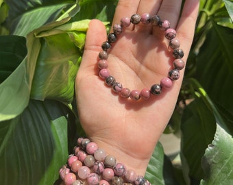 May include: A set of pink and black gemstone bracelets. The bracelets are made of round beads and are stacked on a person's wrist.