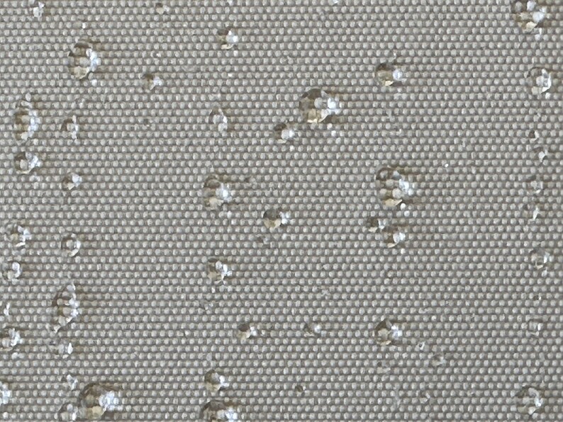 May include: Close-up of a grey, textured fabric with small, white water droplets scattered across the surface.