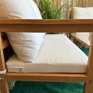 Może przedstawiać: Drewniana sofa ogrodowa z białymi poduszkami. Sofa ma prosty design z plecami i podłokietnikami z listew. Poduszki są grube i wygodne, a sofa jest idealna do relaksu na świeżym powietrzu.