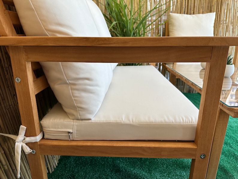 Może przedstawiać: Drewniana sofa ogrodowa z białymi poduszkami. Sofa ma prosty design z plecami i podłokietnikami z listew. Poduszki są grube i wygodne, a sofa jest idealna do relaksu na świeżym powietrzu.