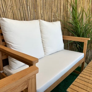 Może przedstawiać: Drewniana dwuosobowa sofa z białymi poduszkami, ustawiona przed bambusową ścianą. Sofa wykonana jest z naturalnego drewna i ma prosty, elegancki design.