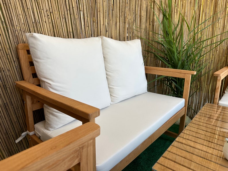 Może przedstawiać: Drewniana dwuosobowa sofa z białymi poduszkami, ustawiona przed bambusową ścianą. Sofa wykonana jest z naturalnego drewna i ma prosty, elegancki design.