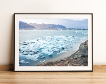 Puede incluir: Una fotografía panorámica de una laguna glacial en Islandia. El agua es de color azul claro y está llena de icebergs. Las montañas en el fondo están cubiertas de nieve.