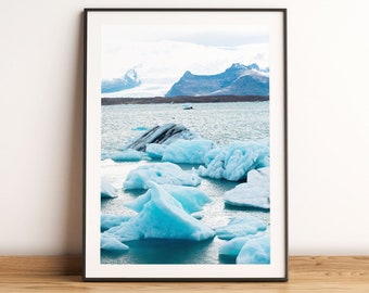 May include: A photograph of a glacial lagoon in Iceland. The water is a bright blue and there are many icebergs floating in it. The mountains in the background are covered in snow.