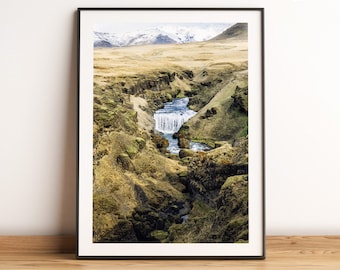 May include: A photograph of a waterfall cascading down a rocky canyon in Iceland. The water is a bright blue and the rocks are covered in green moss. The mountains in the background are snow-capped.