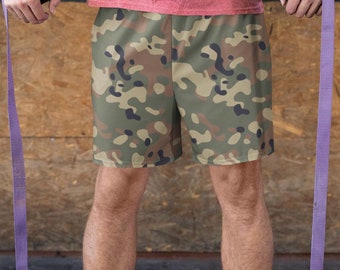 May include: A person wearing a pink t-shirt and camouflage shorts is holding onto gymnastic rings. The rings are attached to purple straps.