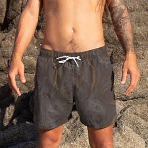 May include: A pair of dark gray swim trunks with a swirling pattern. The trunks have a white drawstring and are made of a lightweight fabric.