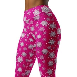 May include: Hot pink leggings with a white snowflake pattern. The leggings are high-waisted and feature a repeating design of various snowflake shapes and sizes. The fabric appears to be a stretchy material.