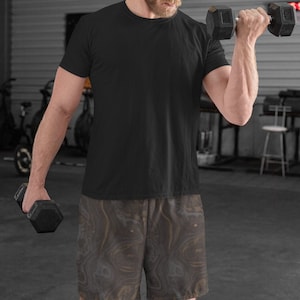 May include: A person wearing a black t-shirt and brown and black patterned athletic shorts. They are lifting a black dumbbell with their right arm.