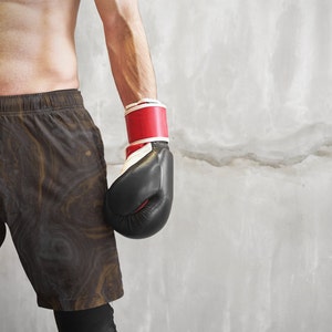May include: A person wearing black and brown patterned shorts with a red and white boxing glove on their left hand.