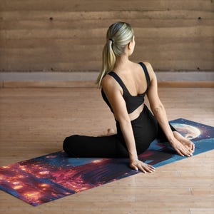 Puede incluir: Una mujer con ropa deportiva negra se sienta en una esterilla de yoga con un dise&ntilde;o de luna y estrellas de colores. La esterilla est&aacute; sobre un suelo de madera.