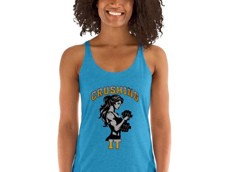 Peut inclure: Un d&eacute;bardeur turquoise avec un graphique d'une femme soulevant des halt&egrave;res. Le texte "CRUSHING IT" est arqu&eacute; au-dessus de la femme en lettres dor&eacute;es et noires. Le d&eacute;bardeur a un design dos nageur.