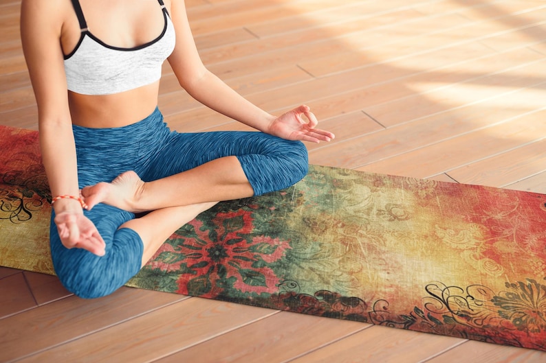 May include: A woman sits in a yoga pose on a patterned yoga mat. The mat has a colorful, vintage-inspired design with floral and geometric patterns in shades of red, yellow, green, and blue.