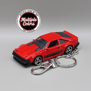 May include: A red sports car keyring featuring a die-cast model vehicle with black detailing, silver wheels, and a metal lobster clasp. A circular graphic above the car displays the text Available In Multiple Colors Options.