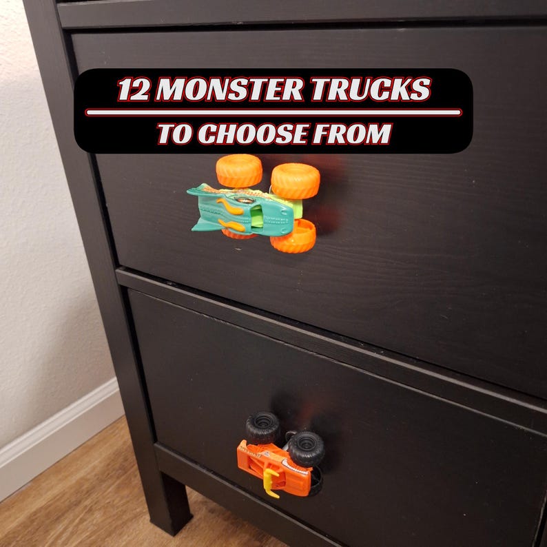 May include: Black chest of drawers with two monster truck drawer pulls. The top drawer has a teal and orange monster truck. The bottom drawer has an orange monster truck. Text on the top of the dresser reads "12 MONSTER TRUCKS TO CHOOSE FROM."