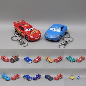 Könnte beinhalten: Eine Sammlung von Miniatur-Spielzeugautos mit verschiedenen Charakteren aus der Cars-Reihe, darunter rote Rennwagen mit der Nummer 95, blaue Sportwagen, ein brauner Abschleppwagen und weitere bunte Fahrzeuge, teilweise an Metallschlüsselanhängern befestigt.