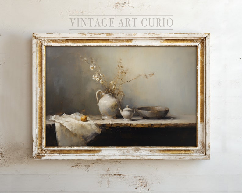 May include: A still life painting in a white frame with gold accents. The painting depicts a white ceramic pitcher with a bouquet of white flowers, a small white teapot, a wooden bowl, and a single orange fruit on a white tablecloth.