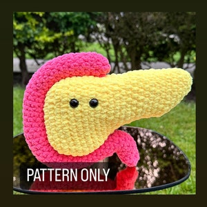 May include: A crocheted plush toy shaped like a pancreas. The pancreas is yellow with a pink top and has two black eyes. The toy is sitting on a black surface.