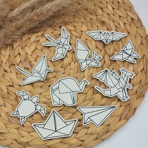 Könnte beinhalten: Ein Set aus zehn schwarzen und weißen Origami-Papierschnitten in verschiedenen Tier- und Formen, darunter eine Fledermaus, ein Vogel, eine Schildkröte, ein Drache und ein Flugzeug. Die Ausschnitte sind auf einer geflochtenen Strohfläche angeordnet.