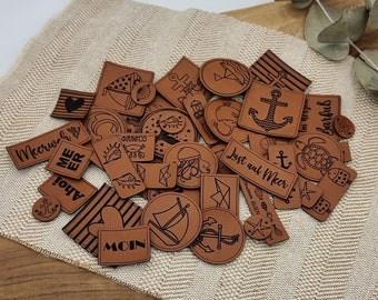 May include: A collection of brown leather patches with various nautical designs and text, including anchors, seashells, fish, and the words "Meer", "Moin", "Lust auf Meer", and "Im Meer barfuß".