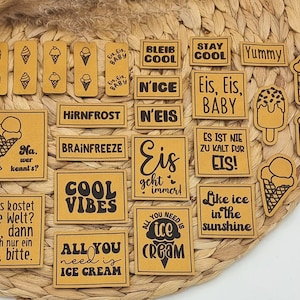 Könnte beinhalten: Eine Sammlung von hellbraunen Lederaufnähern und -ausschnitten mit Eiscreme-Motiven und -Sprüchen. Die Aufnäher zeigen Eistüten, Eis am Stiel und Texte wie "Cool Vibes" und "All You Need Is Ice Cream."