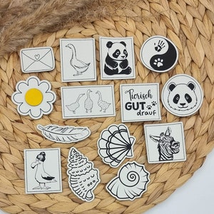 Könnte beinhalten: Ein Set mit 12 schwarz-weißen illustrierten Aufklebern mit verschiedenen Designs, darunter ein Panda, eine Gans, eine Muschel, eine Feder, eine Gänseblümchen, ein Zebra und ein Yin-Yang-Symbol. Die Aufkleber befinden sich auf einem geflochtenen Weidenhintergrund.