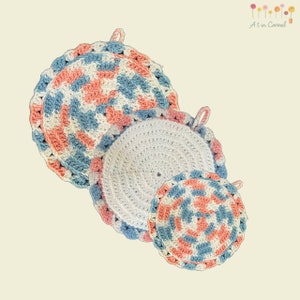 Puede incluir: Tres agarraderas de olla de ganchillo en diferentes tamaños. La agarradera de olla más grande es azul y rosa con un centro blanco. La agarradera de olla mediana es blanca con un borde azul y rosa. La agarradera de olla más pequeña es azul y rosa con un centro blanco.