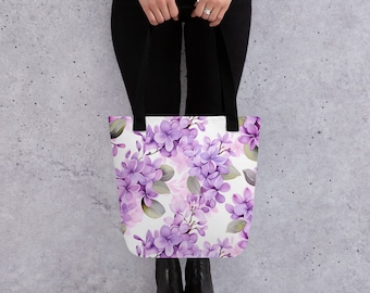 May include: A white tote bag with a floral pattern of purple and pink flowers. The bag has black handles.