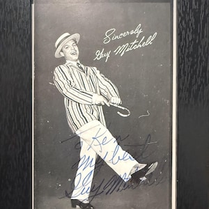 May include: Black and white framed photograph of Guy Mitchell, a singer, in a striped suit and hat, holding a cane. The photo includes the inscription "Sincerely Guy Mitchell" and a signature.