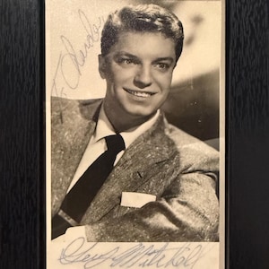 May include: Black and white framed photograph of a smiling man in a suit and tie. The photograph is signed in cursive. The frame is black.