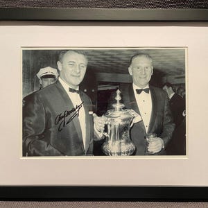 May include: Black and white photo of two men in suits holding a silver trophy. The man on the left is holding the trophy and has signed the photo "Gary Player".