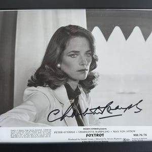 May include: Black and white framed photograph of Charlotte Rampling, signed. The image features Rampling in a blazer, with the film title "Foxtrot" and cast credits at the bottom. The photograph is in a black frame.