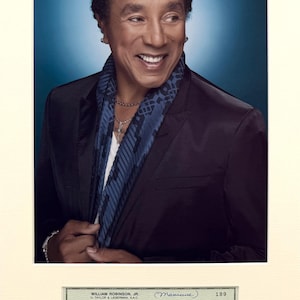 May include: A portrait of Smokey Robinson wearing a dark blazer, a white shirt, and a blue patterned scarf, paired with a City National Bank cheque issued by William Robinson, Jr. to Lois Harris for fifteen dollars, dated 3 April 1991.
