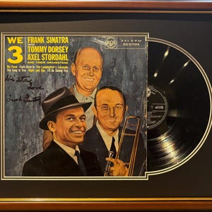 Peut inclure: Un disque vinyle encadré avec une photo en noir et blanc de Frank Sinatra, Tommy Dorsey et Axel Stordahl. Le disque est intitulé "We 3" et comporte le texte "Frank Sinatra with Tommy Dorsey and Axel Stordahl and their orchestras". Le disque est signé par Frank Sinatra.